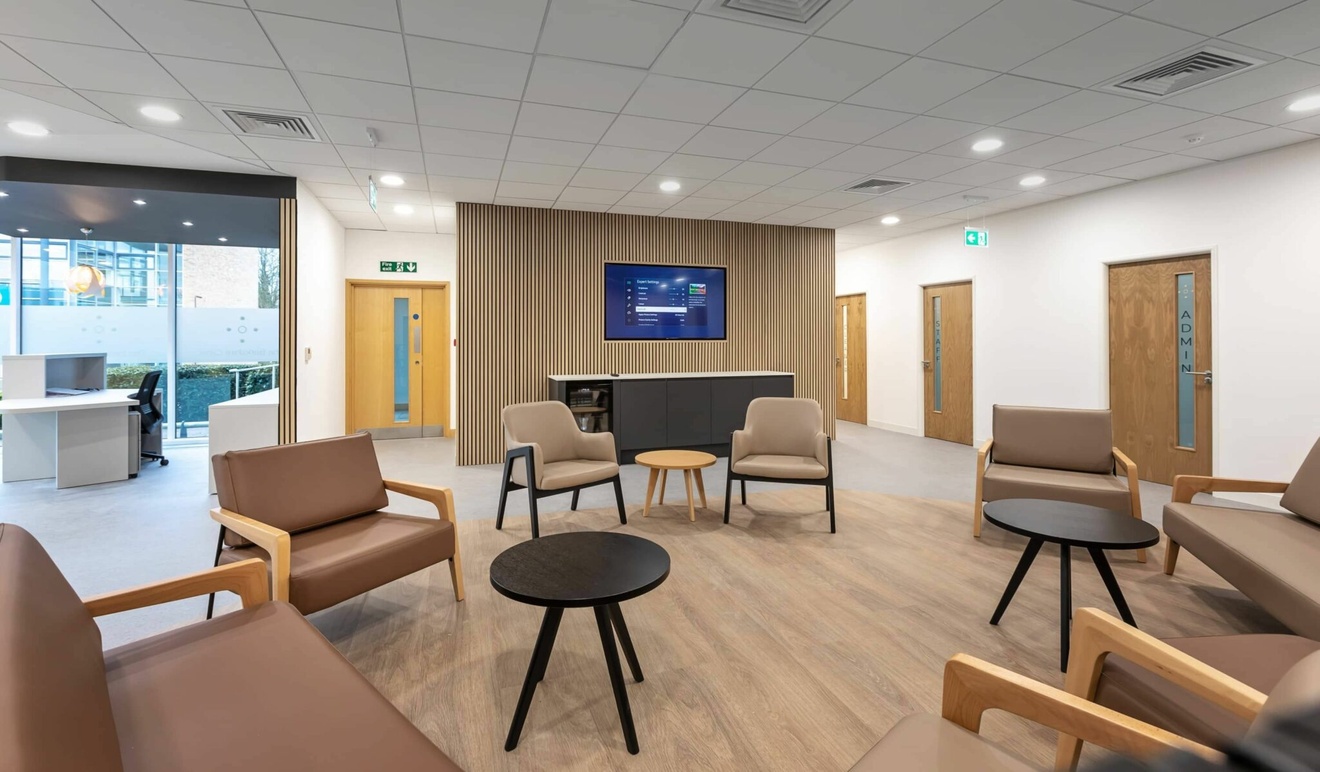 The Berkshire Clinic waiting area a collection of beige sofas and armchairs with a tv on the wall
