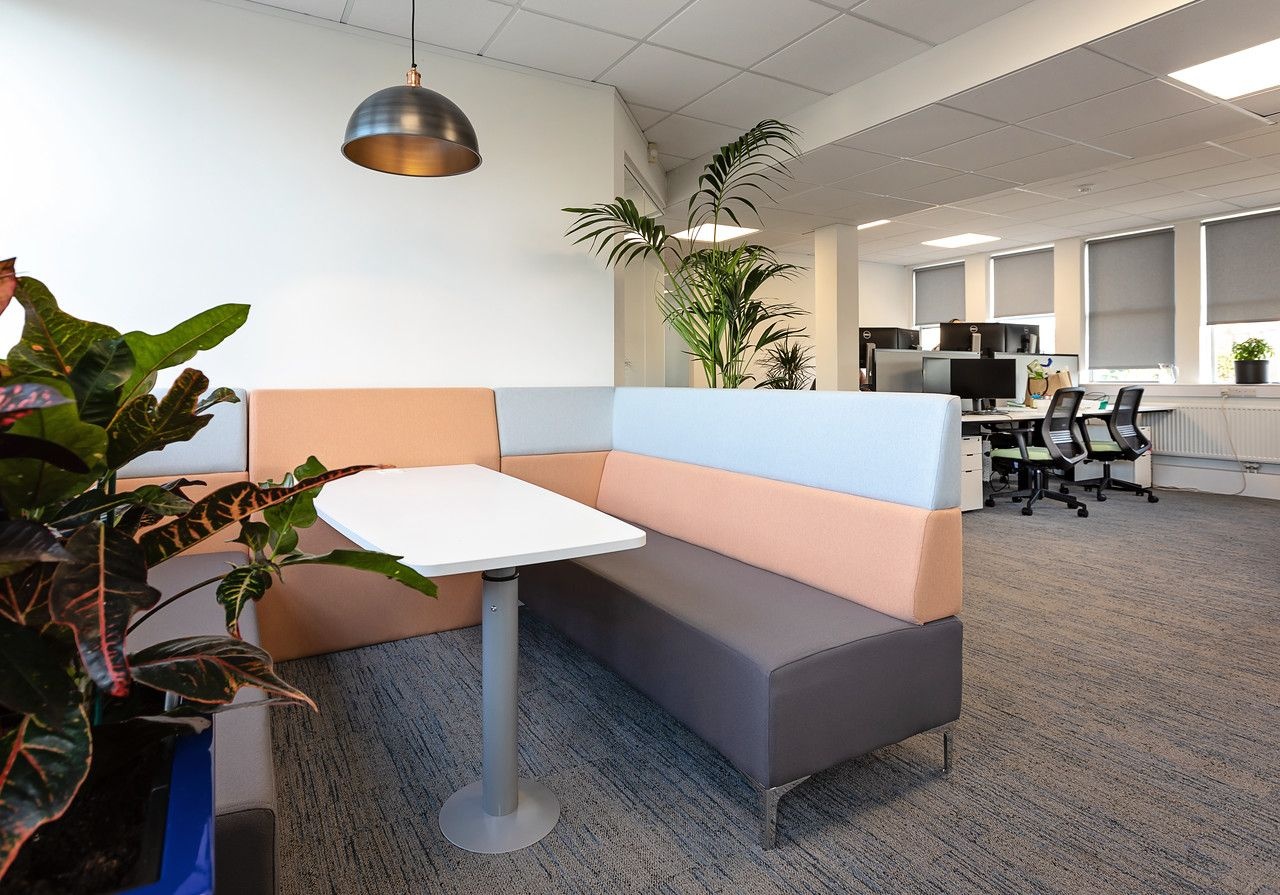 A small sofa area in the corner of an office with a white table in the middle.