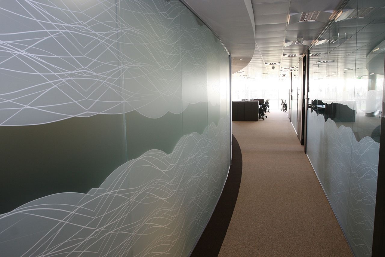 A dark office hallway with glass walls covered in designs.