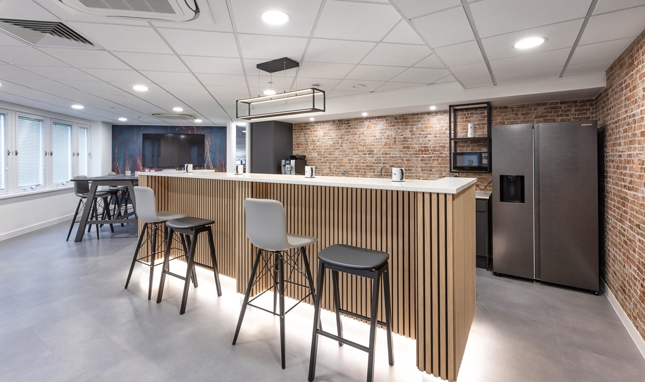 office kitchen and dining area with stools and white countertops with red brick walls