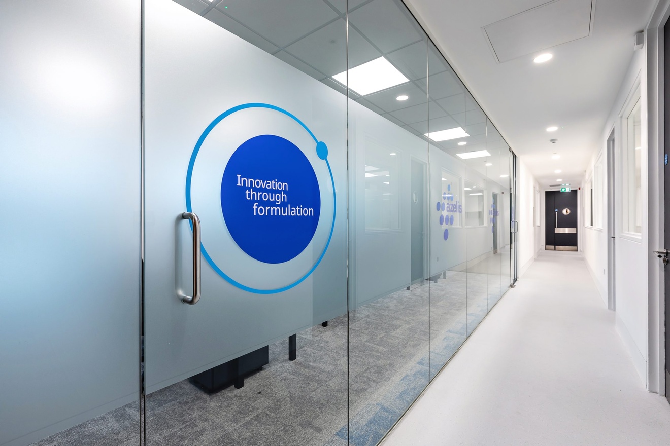 white corridor with a glass left wall with a glass door leading to a meeting room with company logo on the front