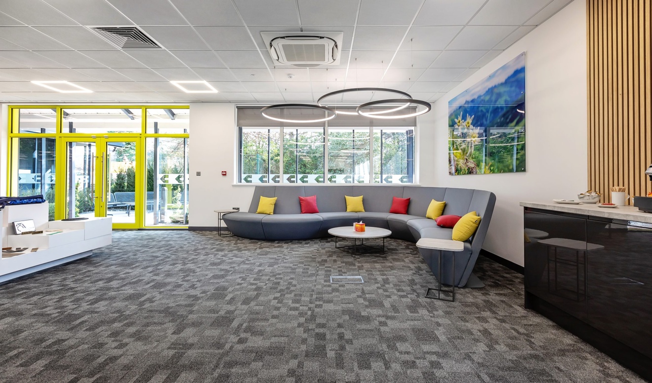 grey s shaped sofa with red and yellow pillows with a coffee machine to the right and product examples to the left