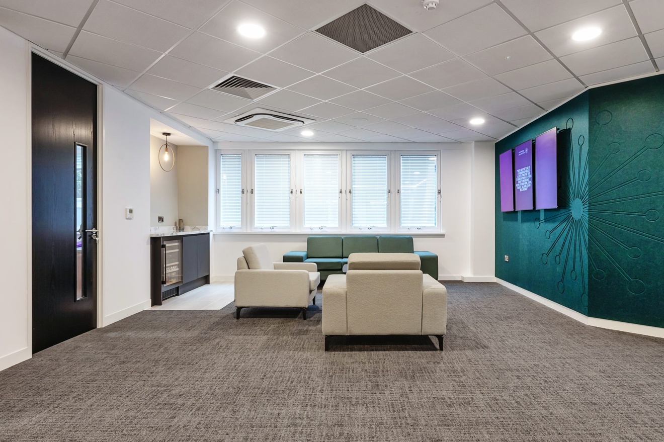 waiting area with white chairs and blue sofa with small fridge to the left and pink signs on the wall