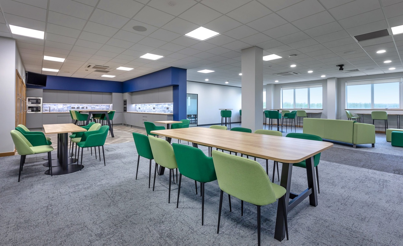 large office lounge and sitting area with green chairs next o kitchen