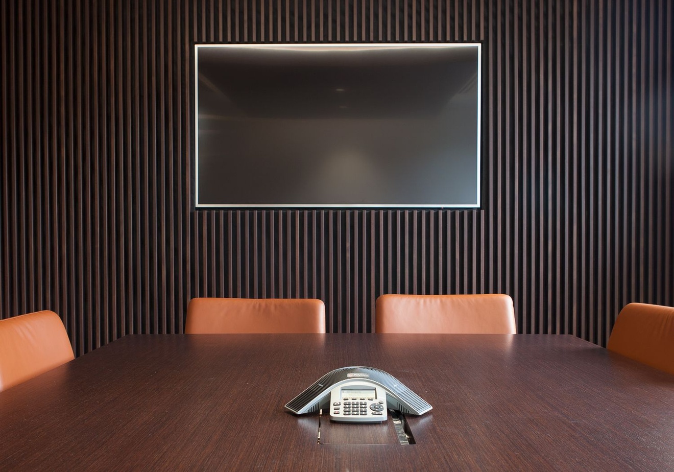 Four chairs at the end of a meeting table with a wall-mounted television behind them.
